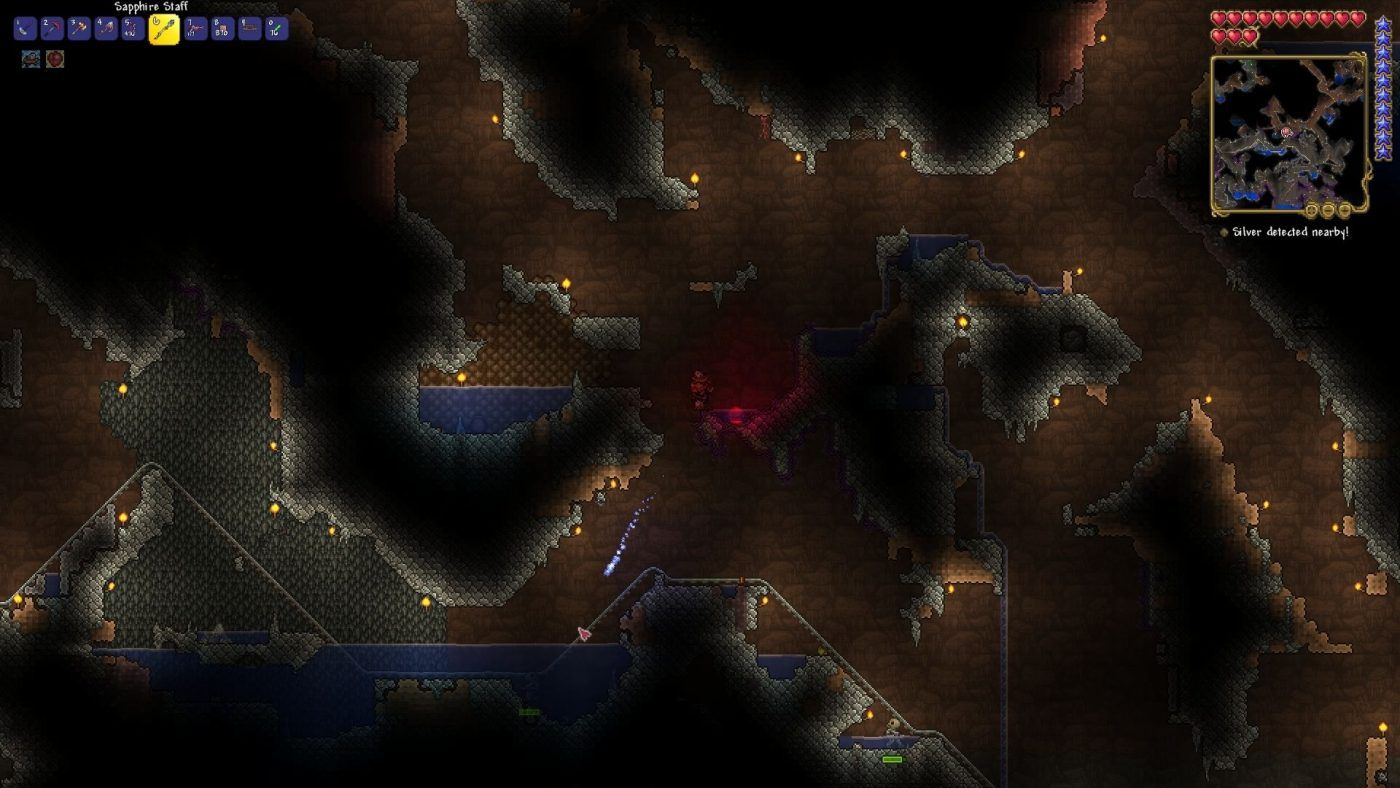A screenshot of Terraria shows the player shooting a blue bolt of magic at a zombie below them in a series of dimly lit tunnels underground.