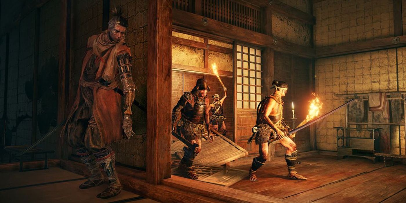 Sekiro hiding against a wall of the interior of a building, as a group of torch-wielding enemies are searching for him. 