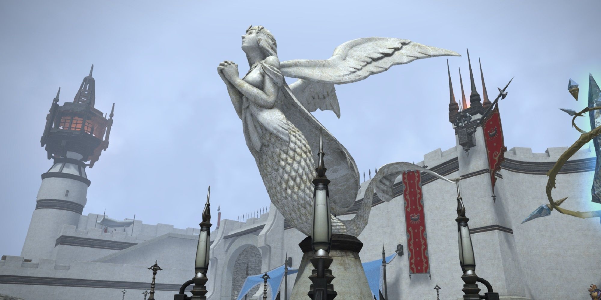 Marble statue of Llymlaen depicted by a praying mermaid with wings. City walls and cloudy sky in the background.