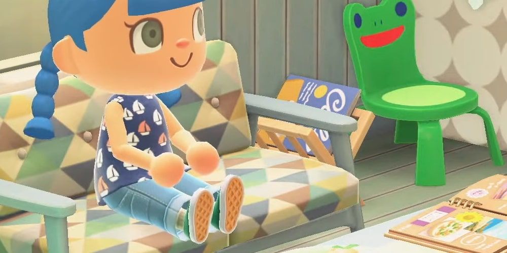 A screenshot of a blue-haired player character wearing a boat patterned shirt and jeans sitting on a seat beside a green Froggy Chair in New Horizons.