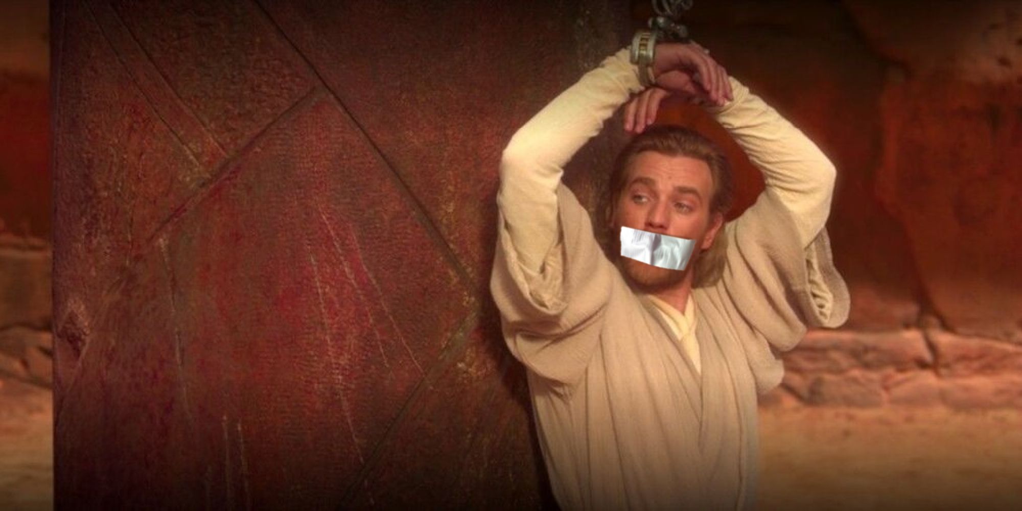 Obi-Wan in a sandy arena, cuffed to a battered stone post with his mouth taped