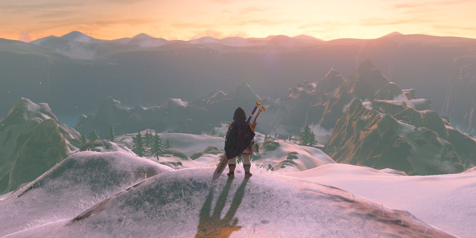 Link on the top of a snowy hill overlooking snow-caked mountain tops during sunset.