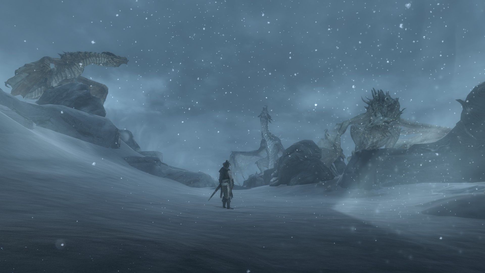 A man stands amidst dragons on top of a snow-swept mountain