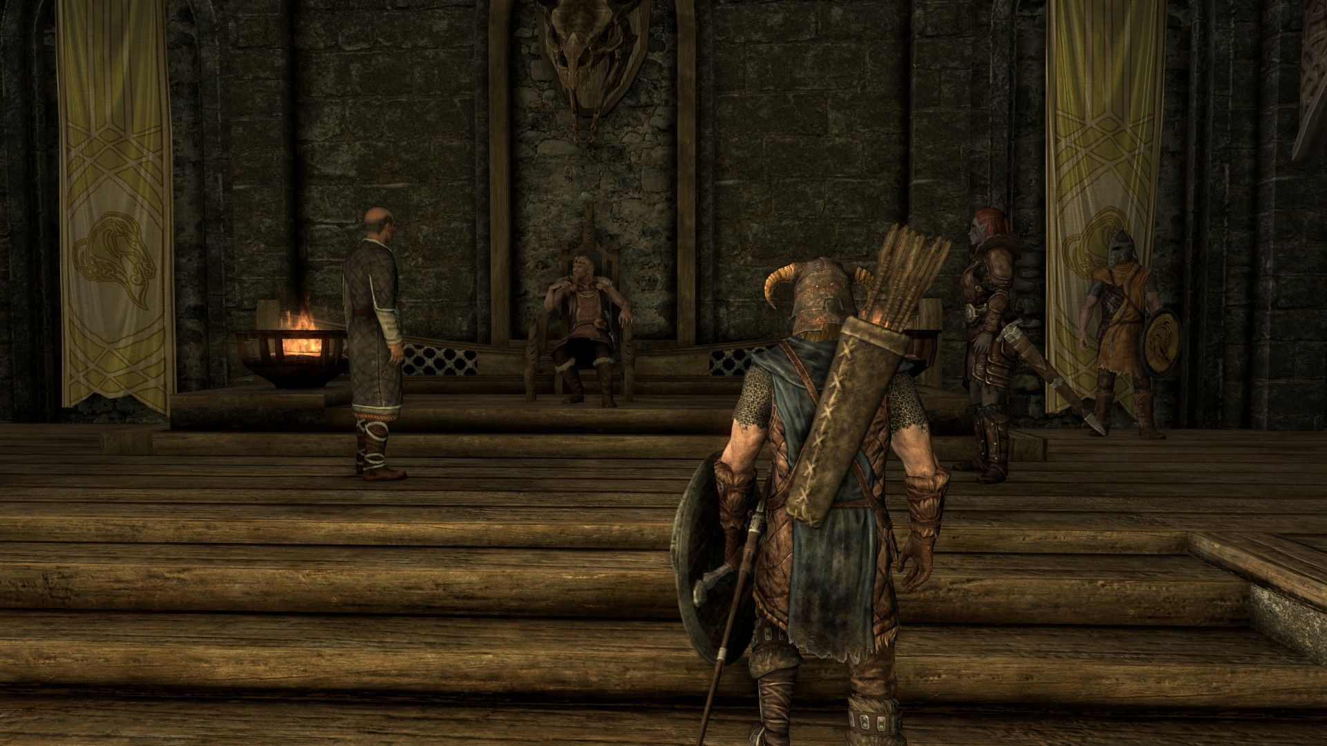 A man approaches a seated lord's throne in a wooden throne room as advisers speak. 