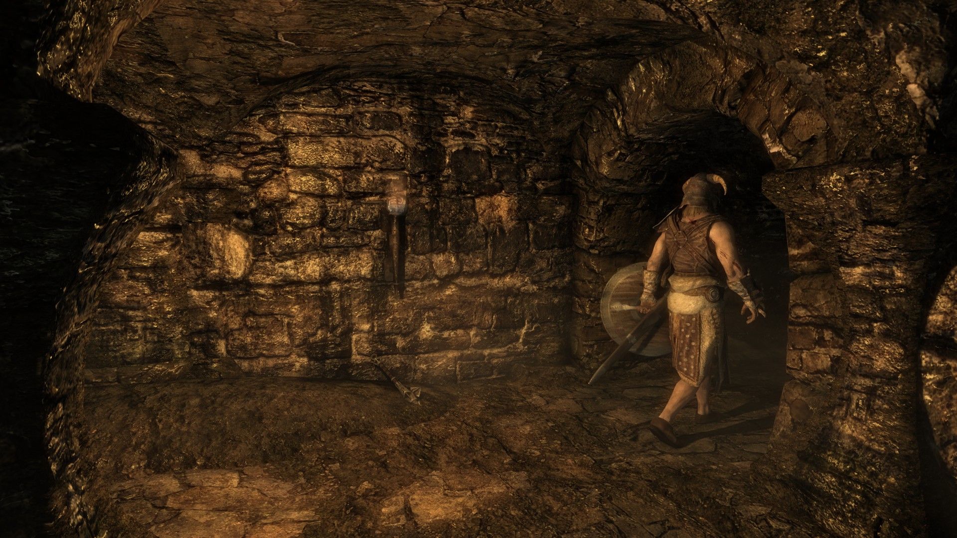 A man walks through a stone tunnel lit by torches