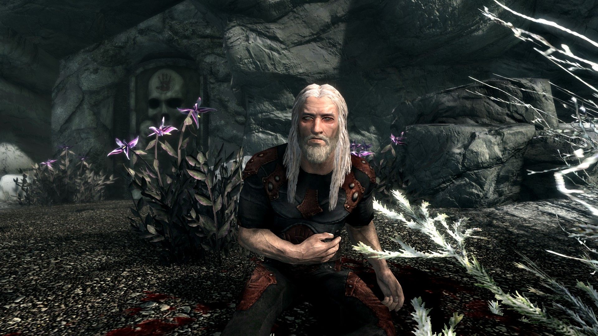 A grizzled man sporting long, white hair clutches his wounded stomach in pain on a snowy coast in front of a menacing door marked with a skull.