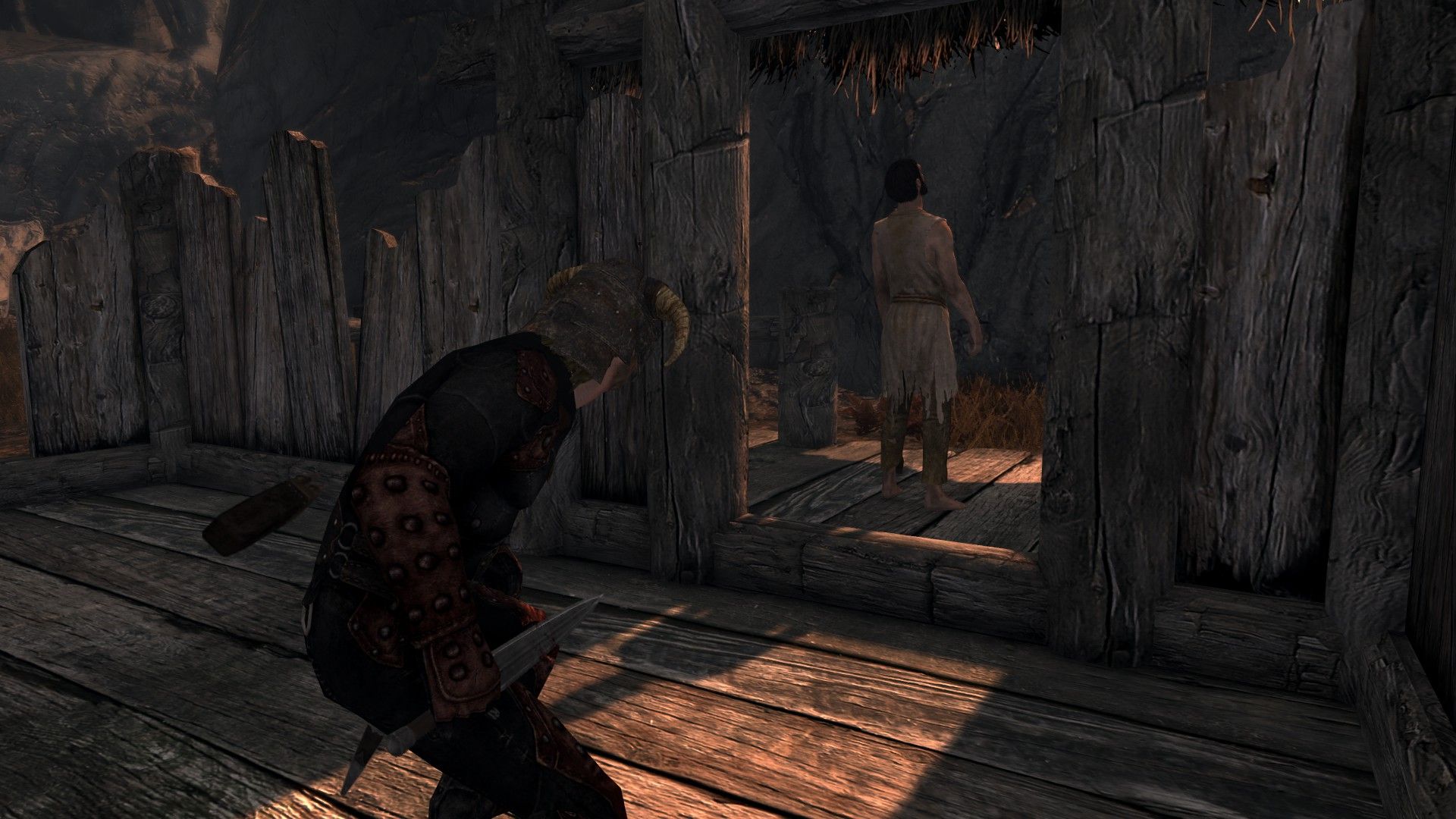 A man sneaks up behind a ragged target in a ramshackle hut.