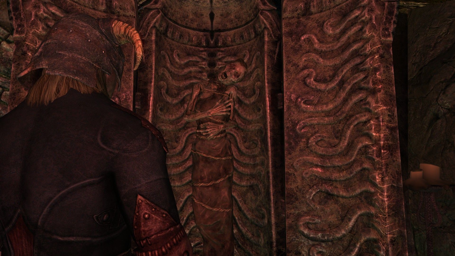 A man looks at a dessicated body held within a metal sarcophagus in a stone room awash with a red glow.