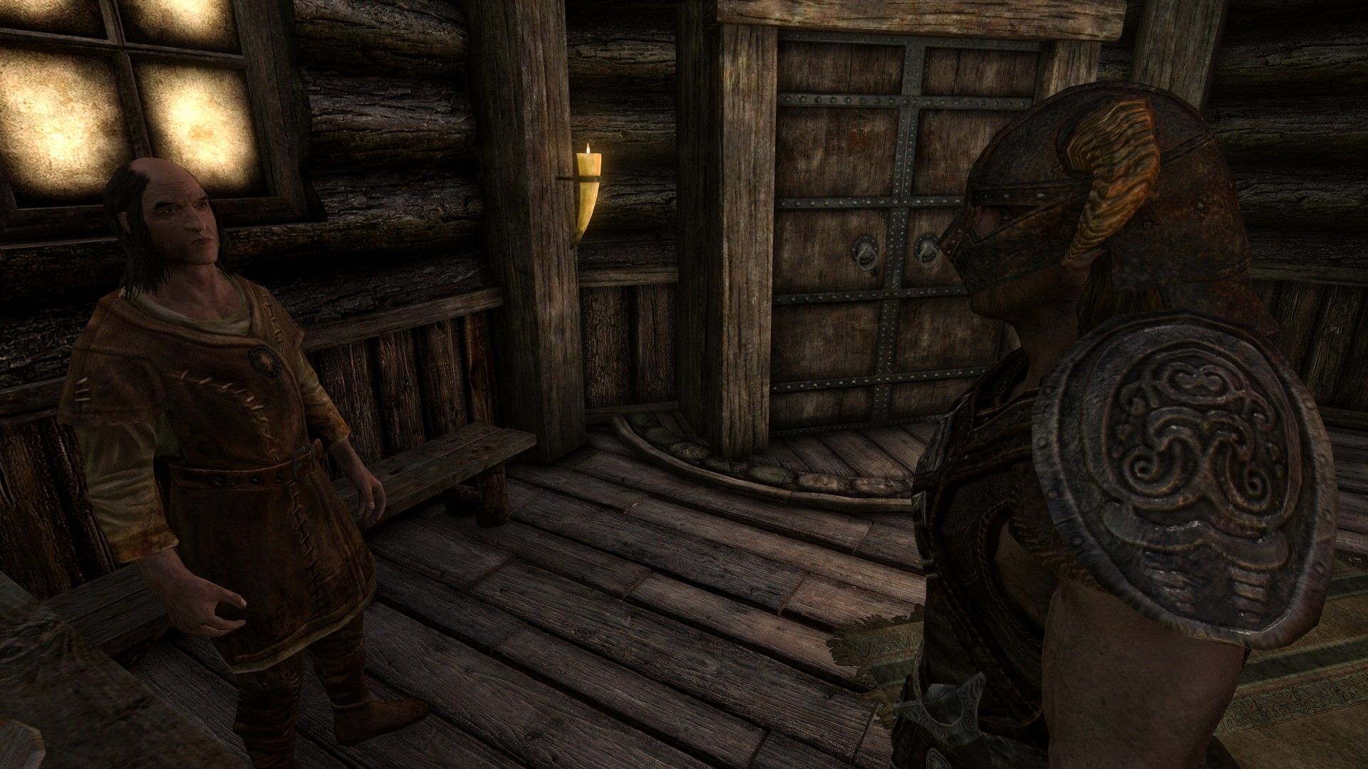 Two men speak by the door of an inn with light coming in from dirty windows and a candle.