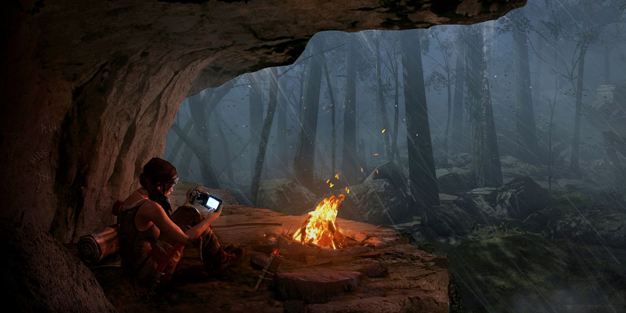 Lara Croft watches Sam's footage on the camcorder as she huddles near the campfire under a rockface