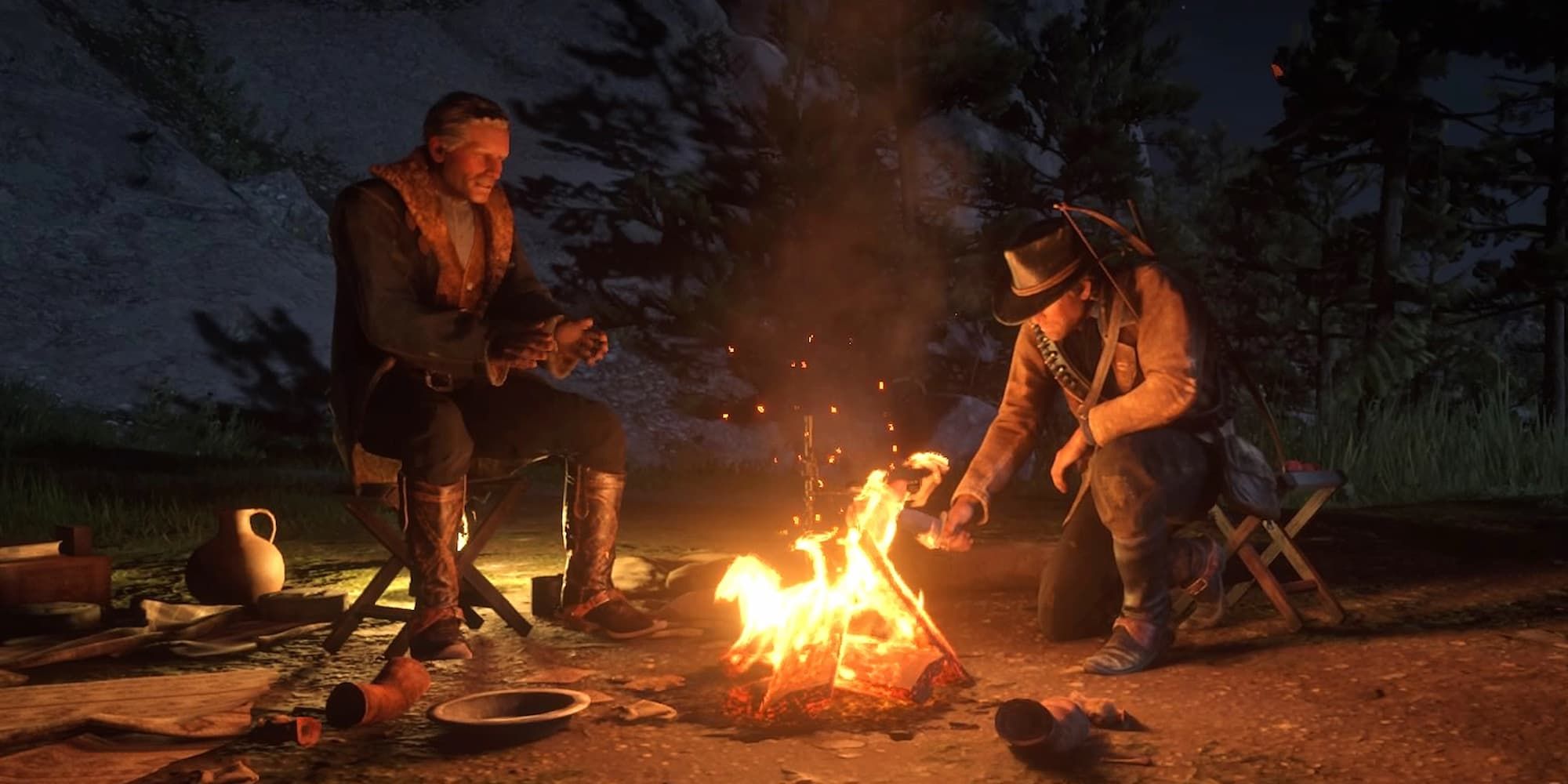 One man warms his hands while the other stokes a fire in Red Dead Redemption 2.