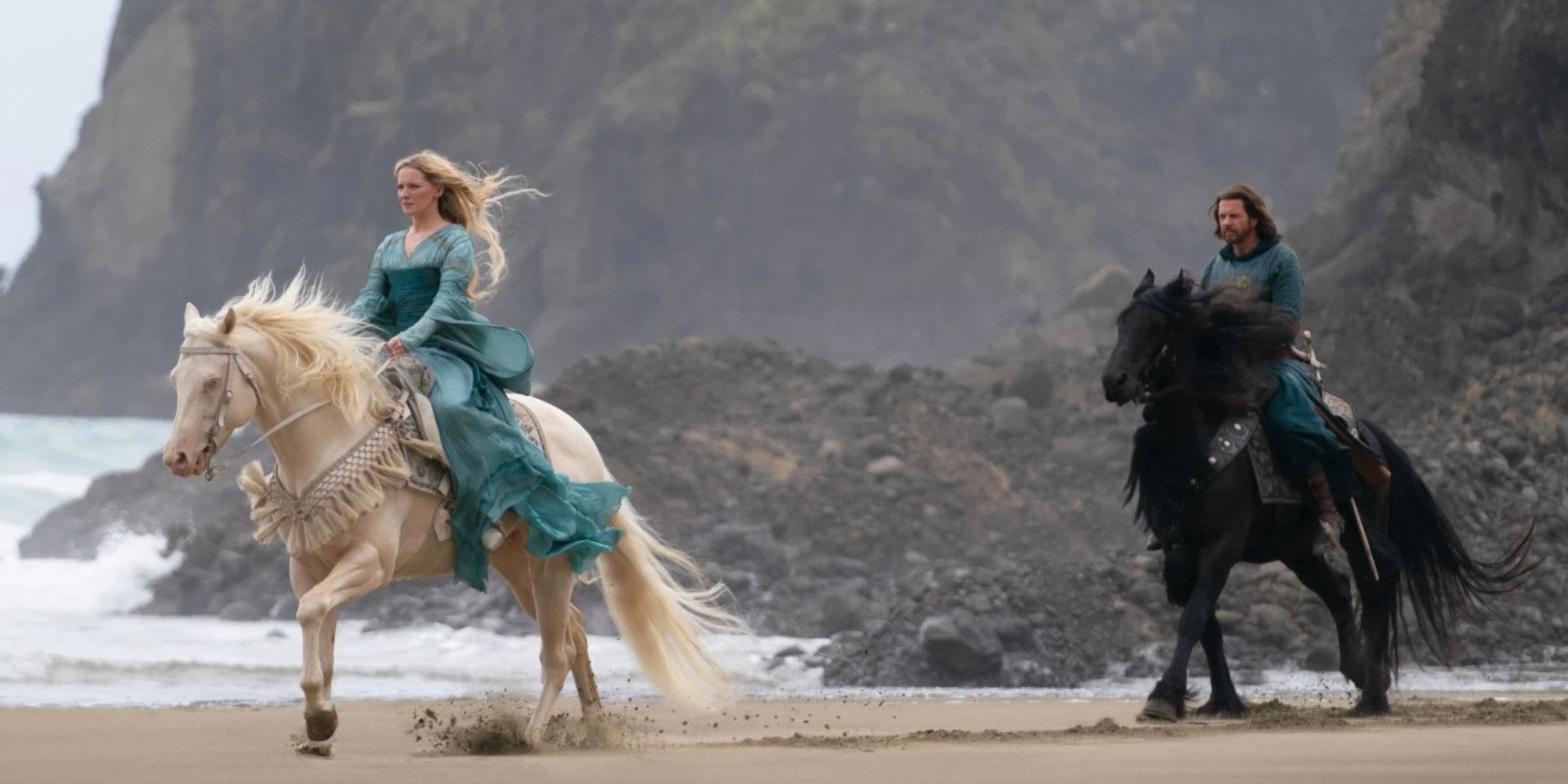 Two people riding horses on a windy beach in Lord of the Rings: The Rings of Power