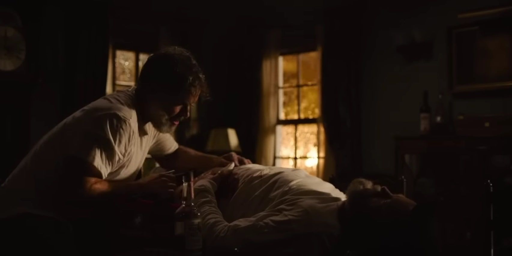 Frank rubbing alcohol into Bill's gunshot wound to the stomach, as he lies in pain on the table.