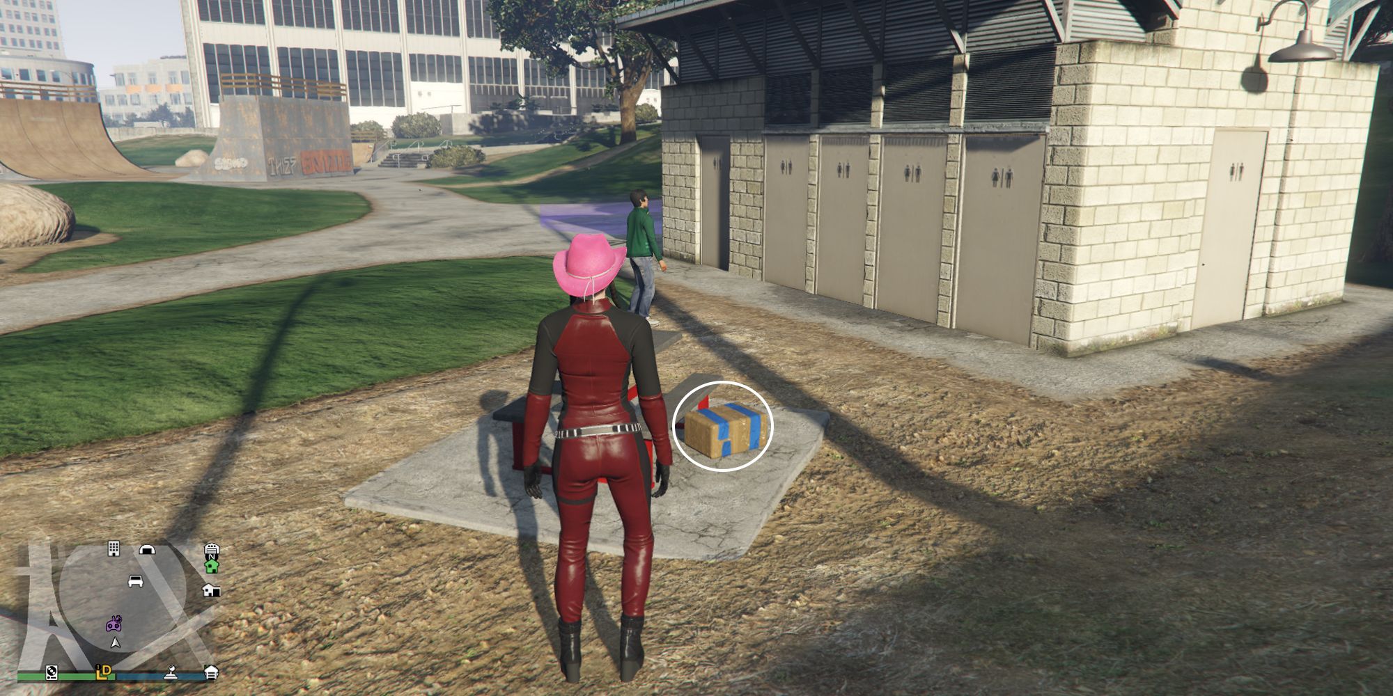Image depicts a female player in GTA Online at Decker Park stood next to another toilet block, with a red bench next to it. In the background there are two skate ramps, and a rock on the left-hand side. G's Cache is sat on the ground next to the red bench.