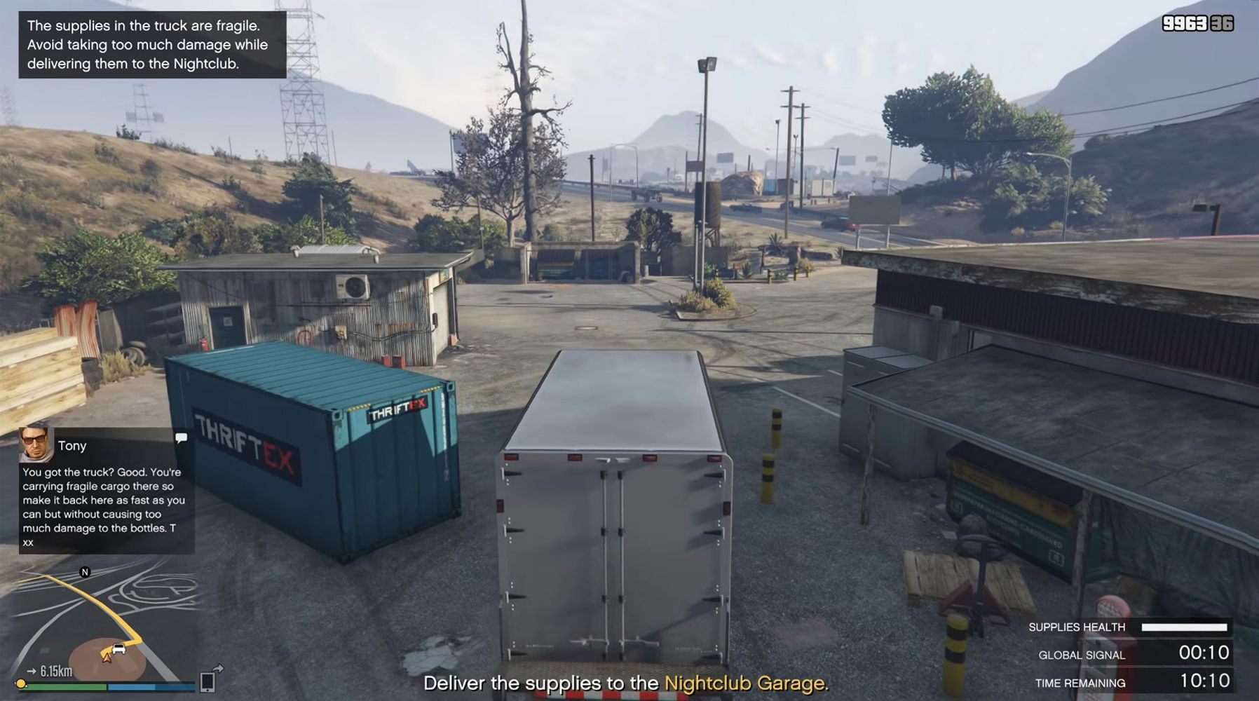 Image depicts a player in Grand Theft Auto Online in a white van next to a blue shipping container. On the left there is a text from Tony that reads 'You got the truck? Good. You're carrying fragile cargo there so make it back here as fast as you can but without causing too much damage to the bottles. T xx'. Above this in the top left it says 'The supplies in the truck are fragile. Avoid taking too much damage while delivering them to the nightclub'. In the bottom centre it reads 'Deliver the su