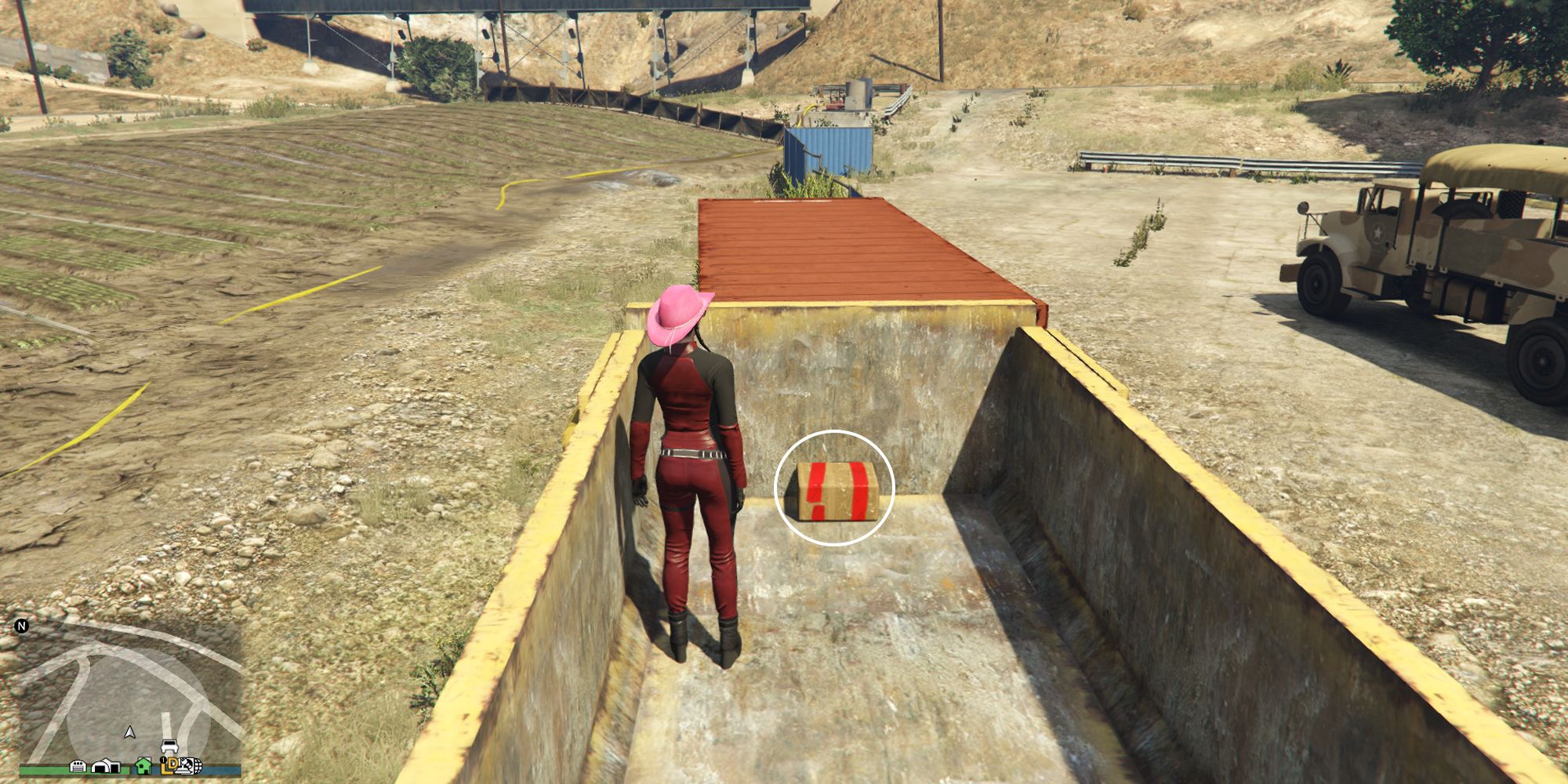 Image depicts a female character in GTA Online at Grapeseed Rail Terminus inside the back of a yellow trailer, with a copper storage container in front of this. Inside the trailer is the G's Cache box.