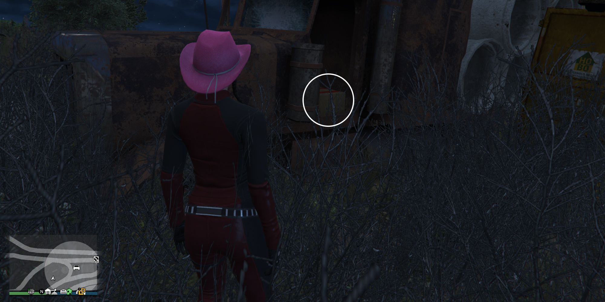 Image depicts a female player in GTA Online at Jay and Sons in El Burro Heights stood in front of an abandoned truck with a flatbed of materials on the back. G's Cache is on the driver seat of this truck.