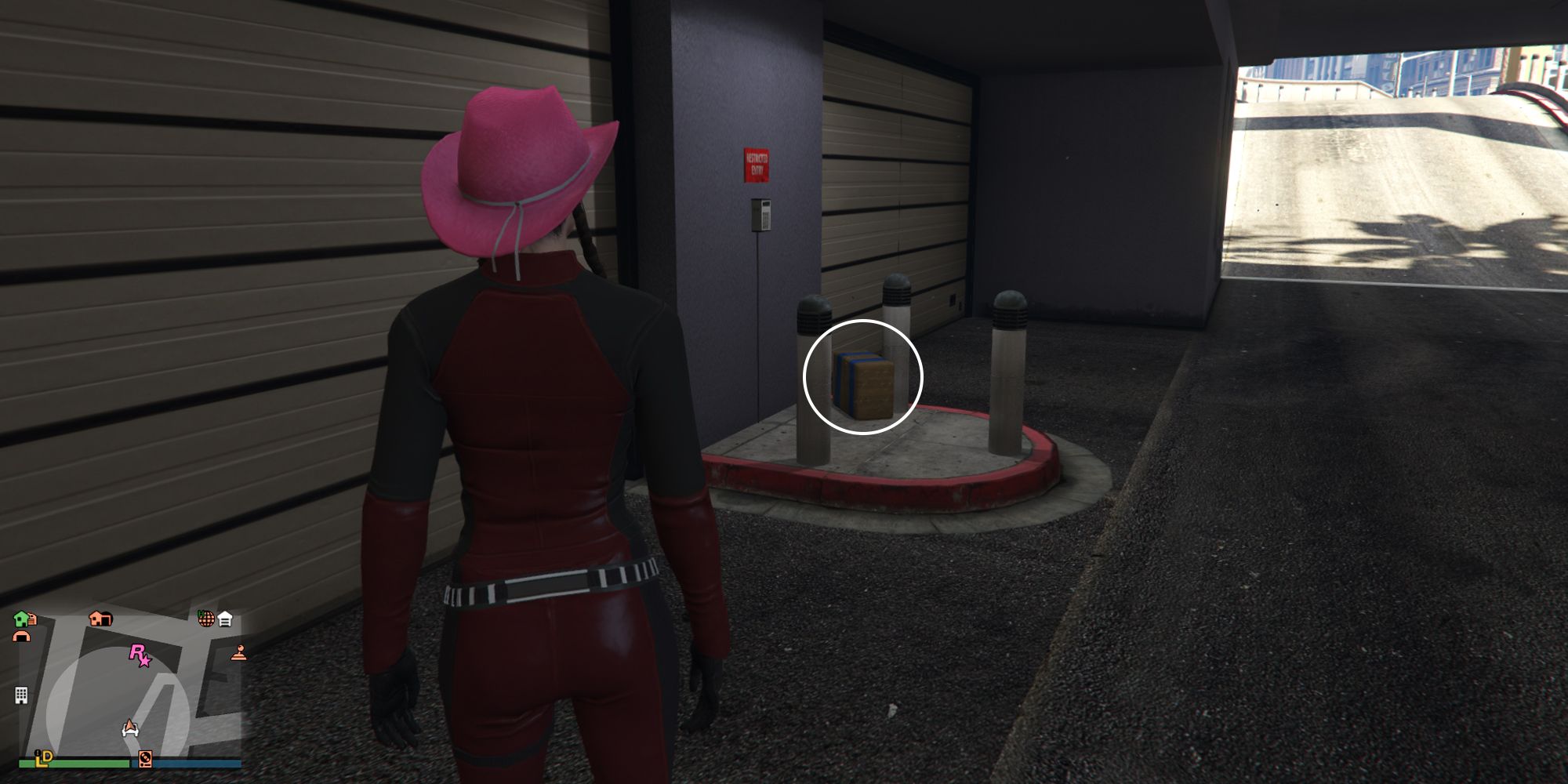 Image depicts a female player in GTA Online at Legion Square underneath the main area outside of a parking garage. In the centre of the garage entrance, there are three pillars, and G's Cache is on the ground next to these.