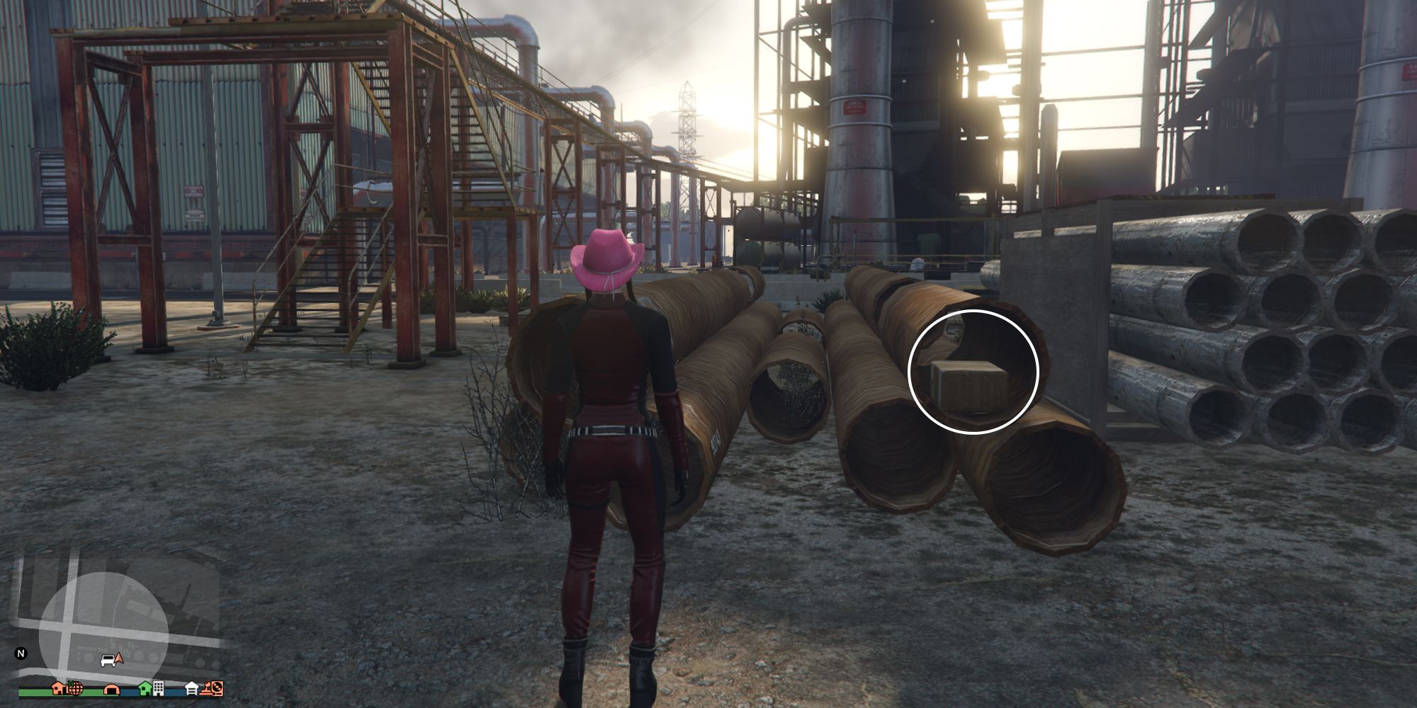 Image depicts a female character in GTA Online at Palmer-Taylor Power Station stood in front of some stacks of metal pipes in a construction yard. In the top pipe on the right-hand stack is the box of G's Cache.