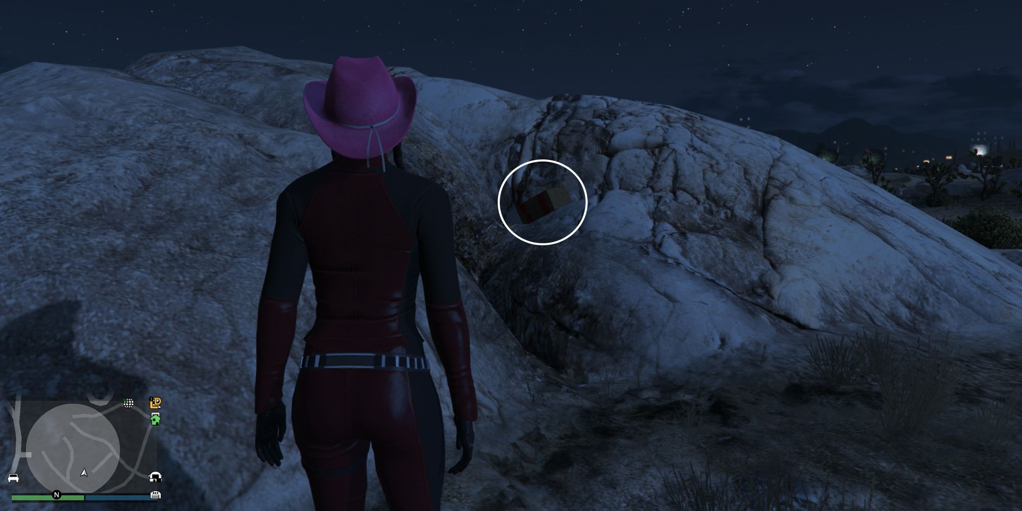 Image depicts a female character in GTA Online at Senora National Park stood in front of a large set of rocks in the desert. There is a small path between two sets of rocks, and G's Cache is on top of this pile.