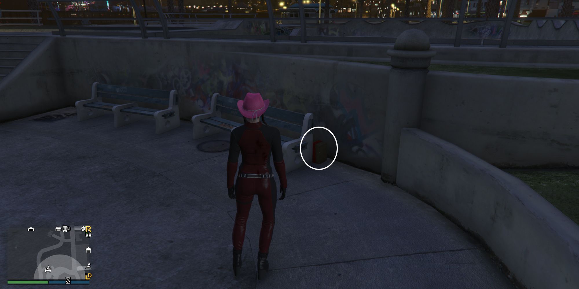 Image depicts a female player in GTA Online at Vespucci Beach Skate Park facing some benches in the main skating area. There are two benches next to each other, with some stairs on the left-hand side. G's Cache is tucked behind the bench on the right.