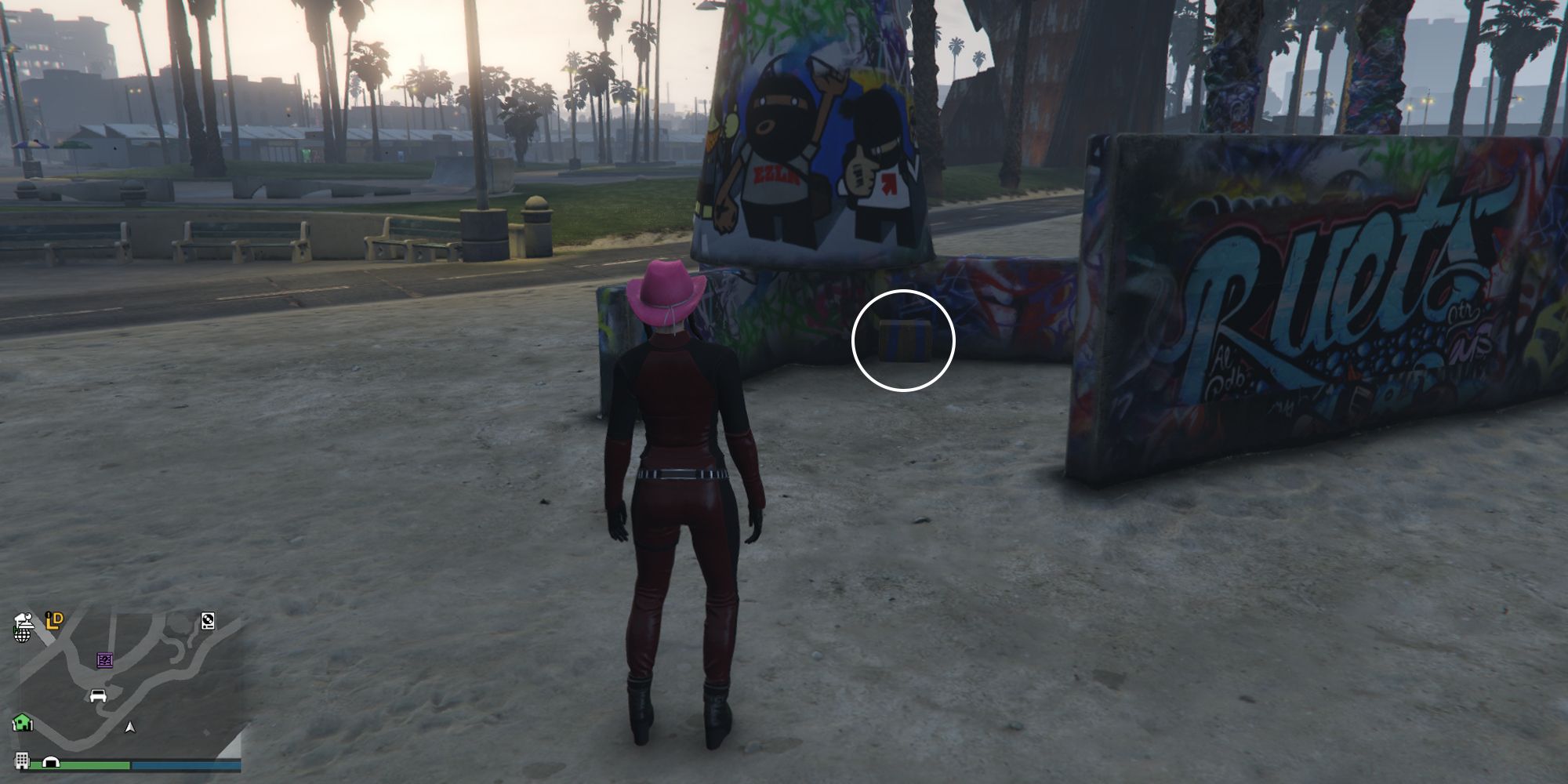 Image depicts a female player in GTA Online at Vespucci Beach Skate Park facing a series of walls that are covered in colourful graffiti. On the right, there is a flat wall, and in the centre there is a pillared wall, split into three different sections. In the space between the sections, G's Cache is on the ground. 