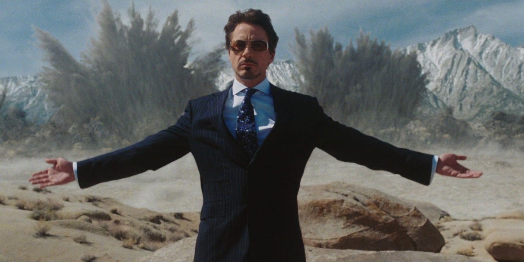 Tony Stark (Robert Downey Jr.) in Iron Man holding his arms out wide as weapons explode behind him