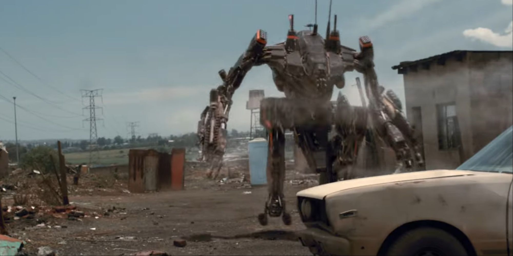 Wikus piloting an exosuit that's charging toward a car to engage enemies in order to protect Christopher Johnson.