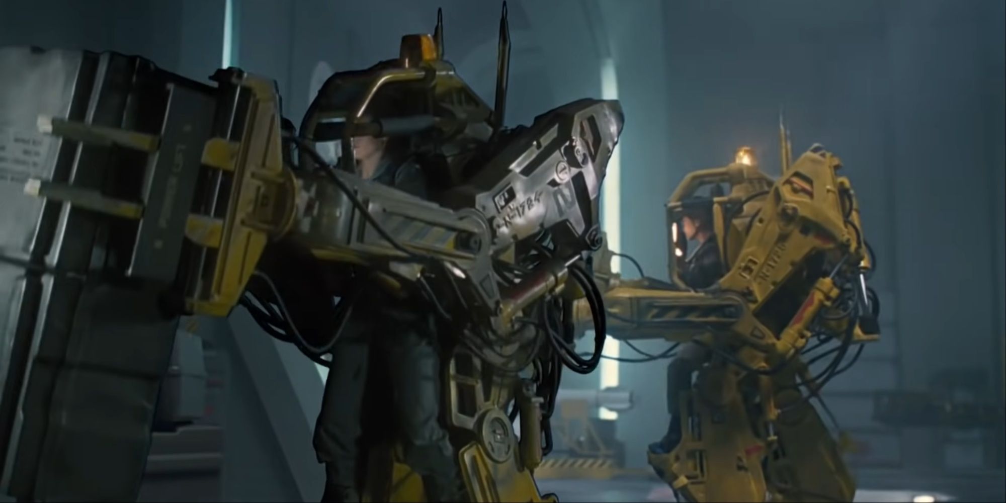 Ripley using the power loader to lift a heavy cargo box, with a fellow crewmate doing the same beside her.