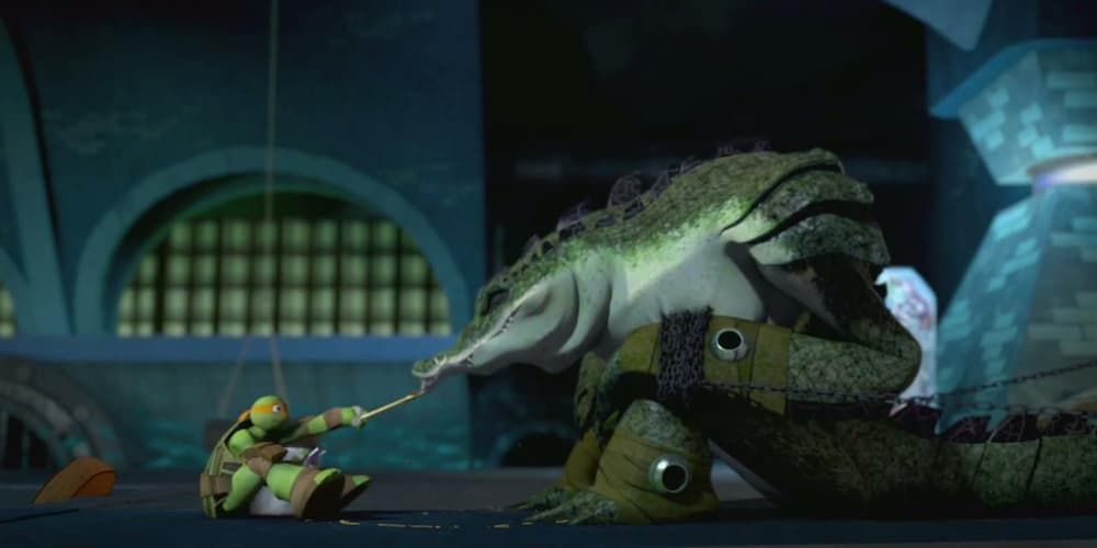 Michelangelo sits and feeds Leatherhead as he is chained to a wall.