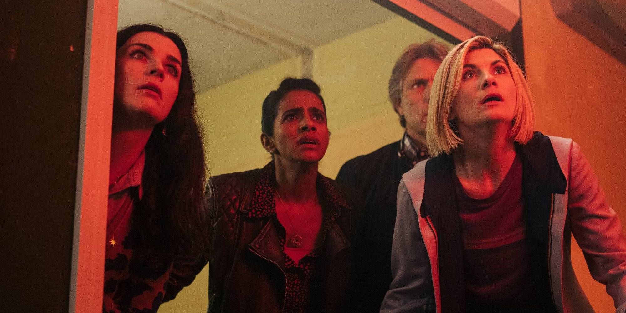 The Doctor and companions looking shocked whilst in a room bathed in red light