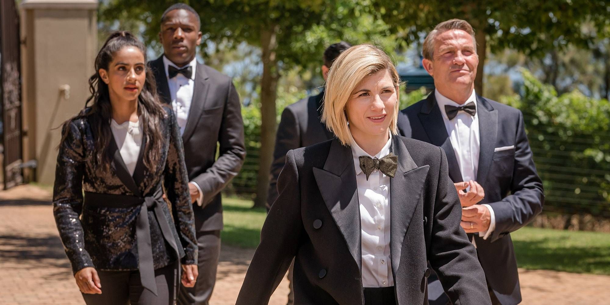 The Doctor and their companions walking in black suits