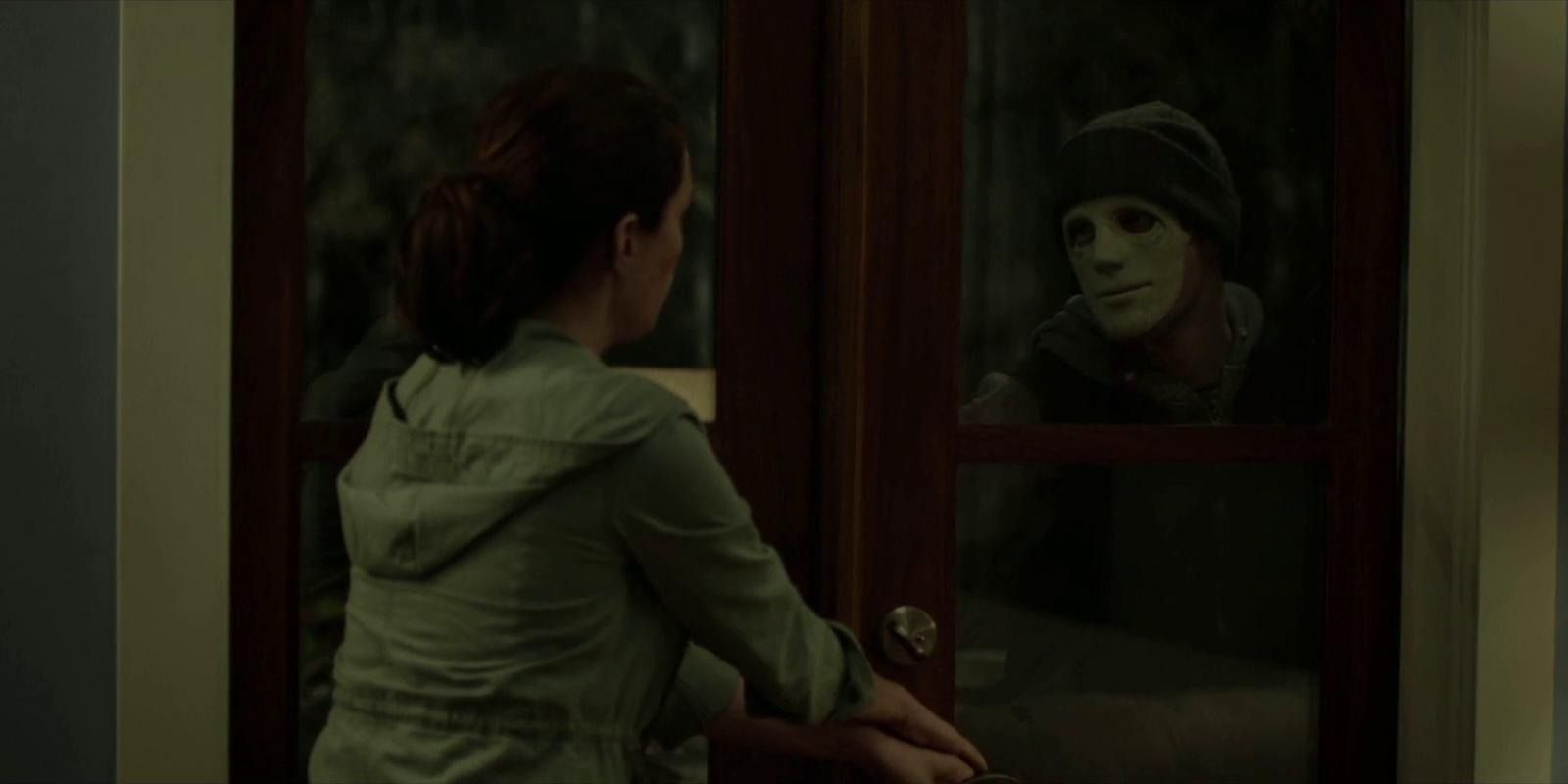 Hush - Maddie holding her front door closed as the masked Intruder watches her