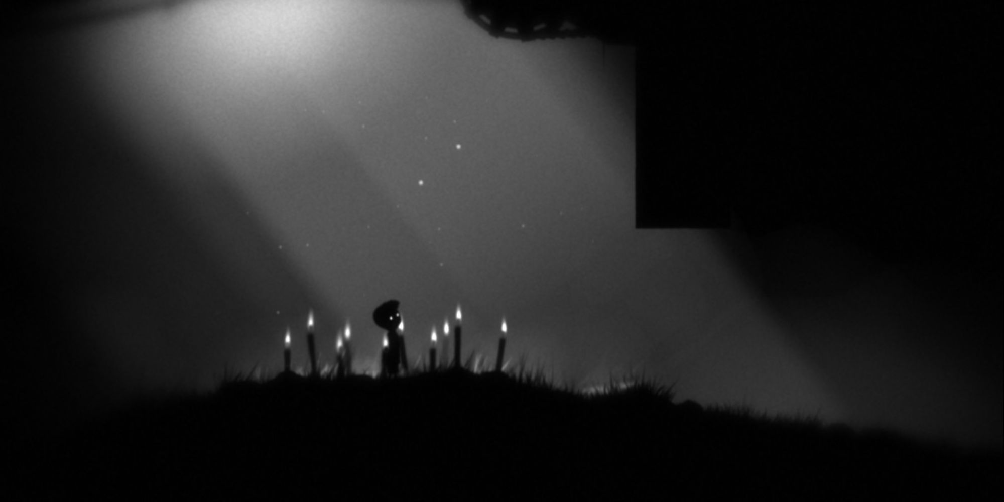 A shadowy image of the silhouette of a boy surrounded by multiple lit candles.