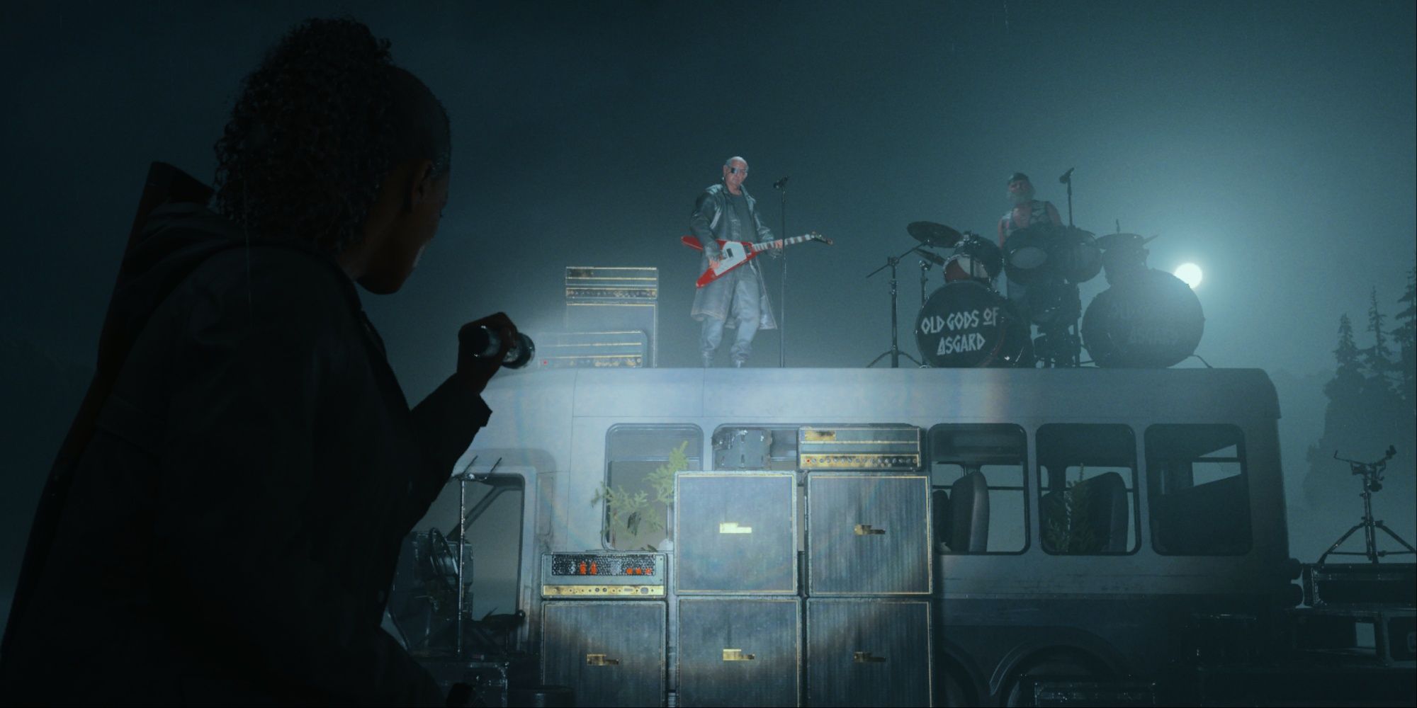 Saga pointing her flashlight at Tor and Odin, who are on top of a bus ready to rock out on the guitar and drums.