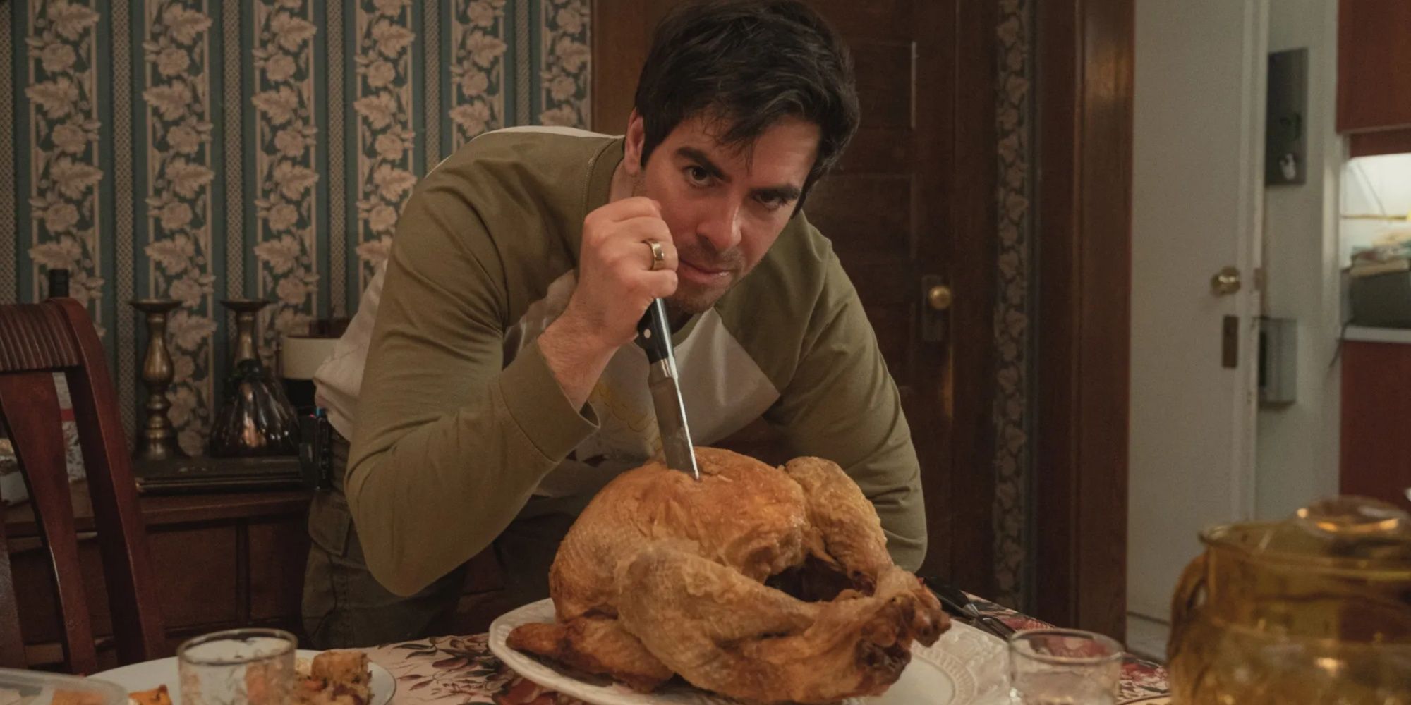 A man menacingly looms over a cooked turkey after stabbing it with a kitchen knife.