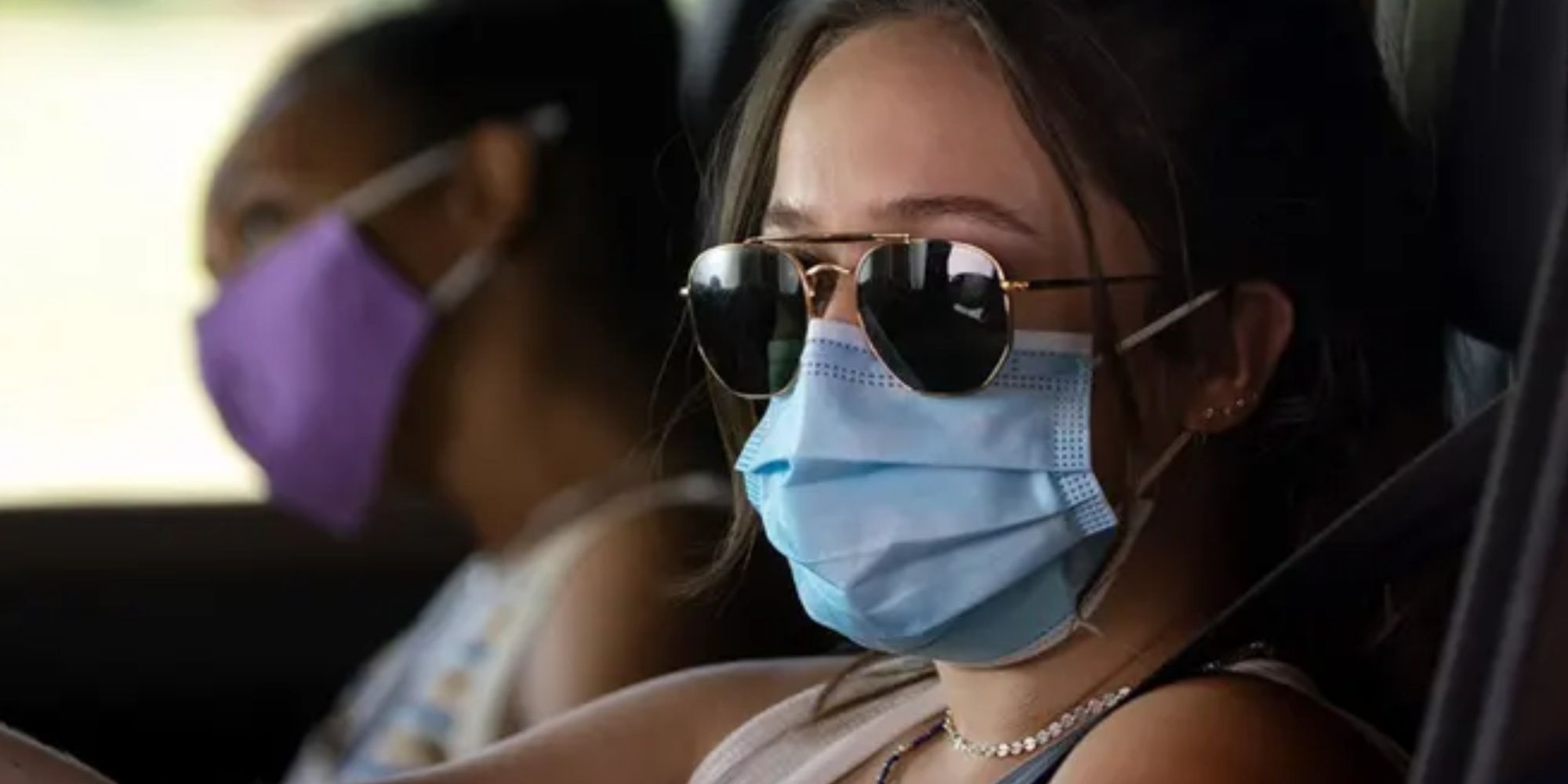 Two young women in protective masks, driving in a car during the Covid pandemic.