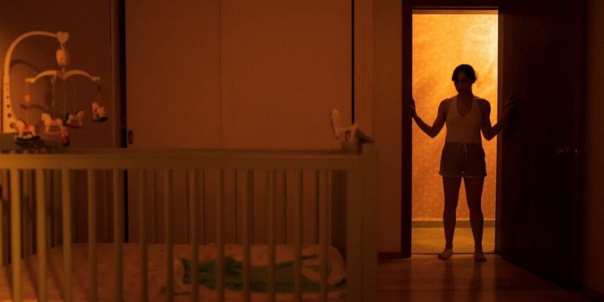A woman stands in the doorway to a room, looking at an empty crib.