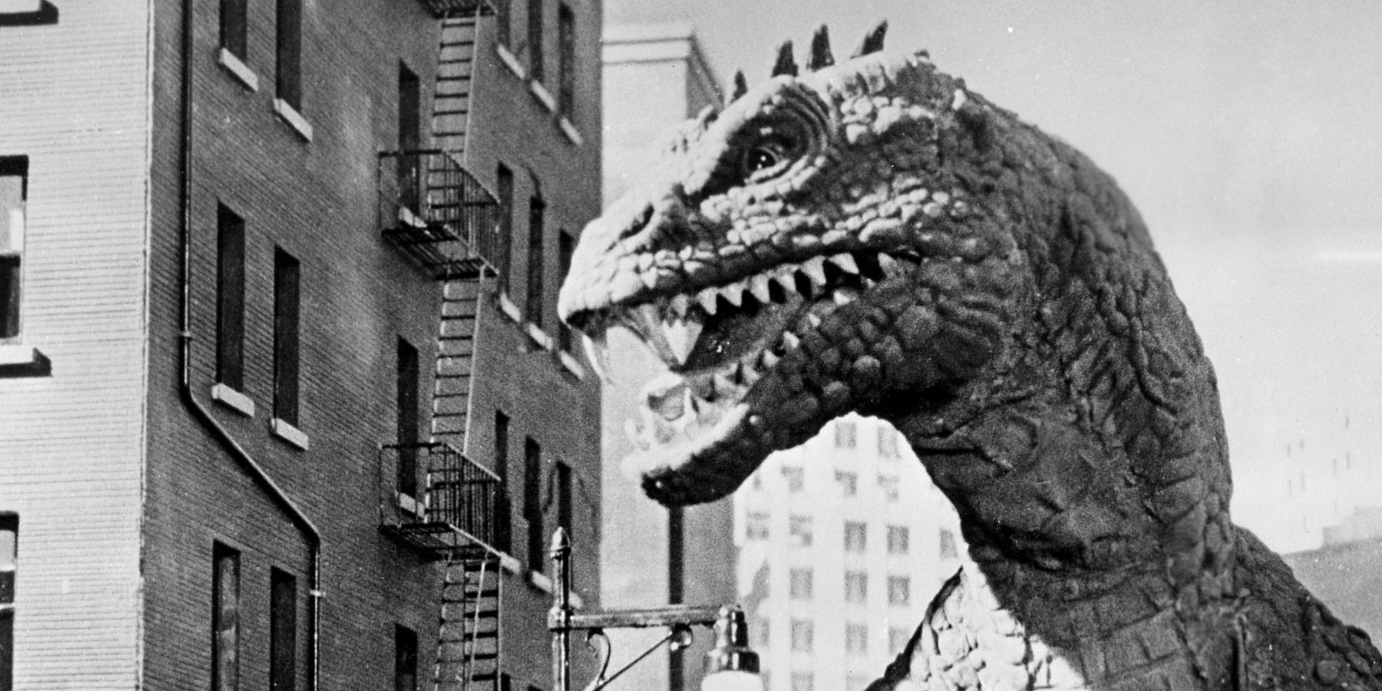 A still from the black and white movie, The Beast from 20,000 Fathoms, featuring the titular lizard monster next to a building.