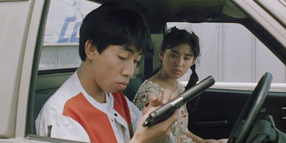 Characters in a car, one of them holding a gun