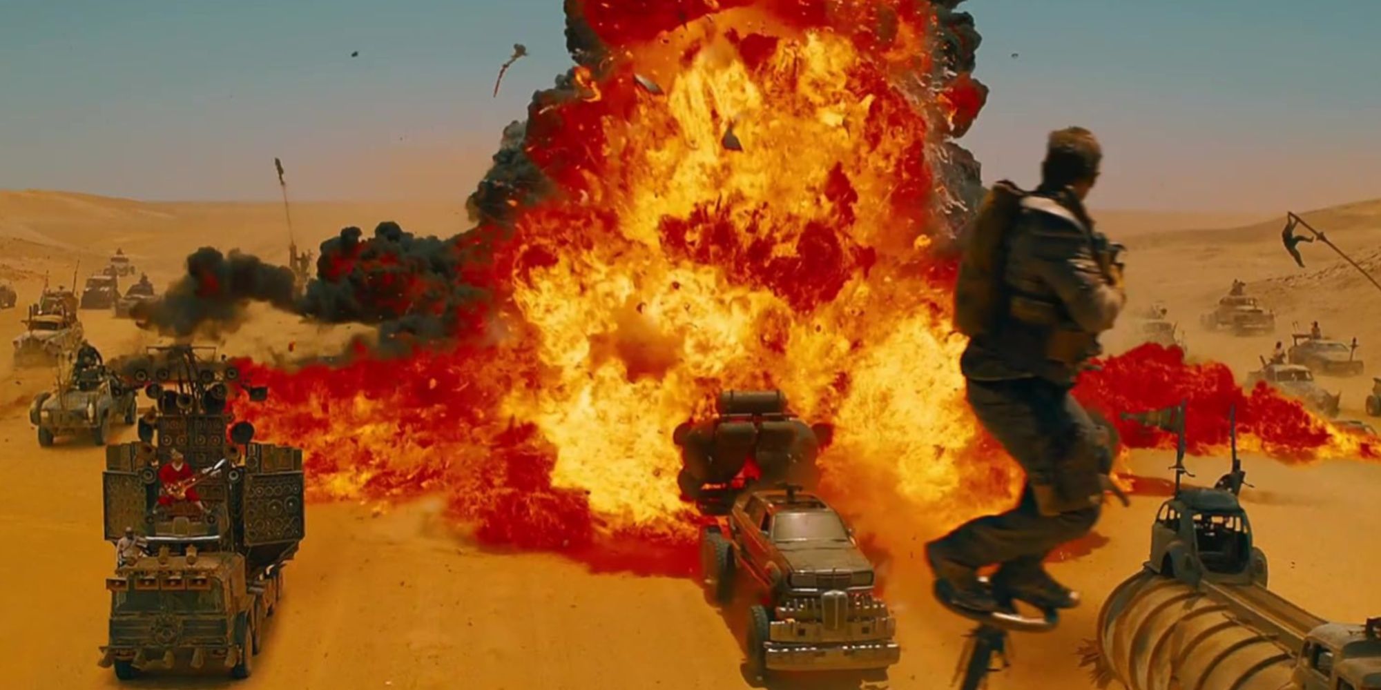 Max suspended in the air by being tied to a pole, as a giant explosion engulfs the nearby cars on the desert road.
