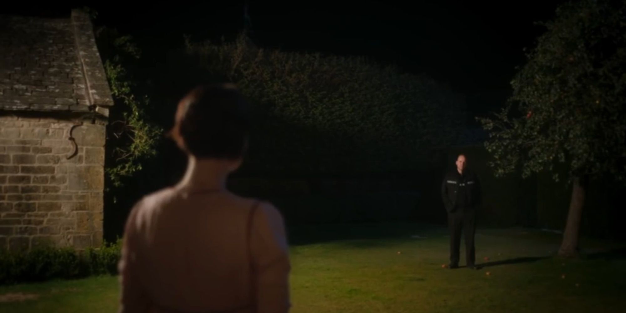 Jessie Buckley with her back to the camera staring at Rory Kinnear's menacing appearance on her cottage yard, with some fallen apples from the tree.