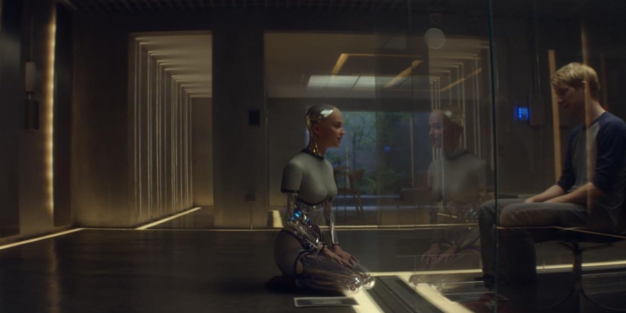 Caleb sitting on a chair on the other side of a glass screen chatting with Ava, on her knees inside her room.