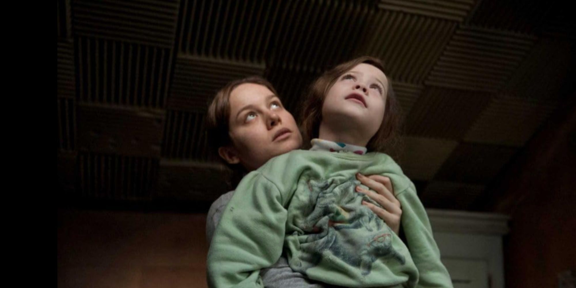 Brie Larson holding her on-screen son Jack as he stares up at the ceiling with an expression of wonder.