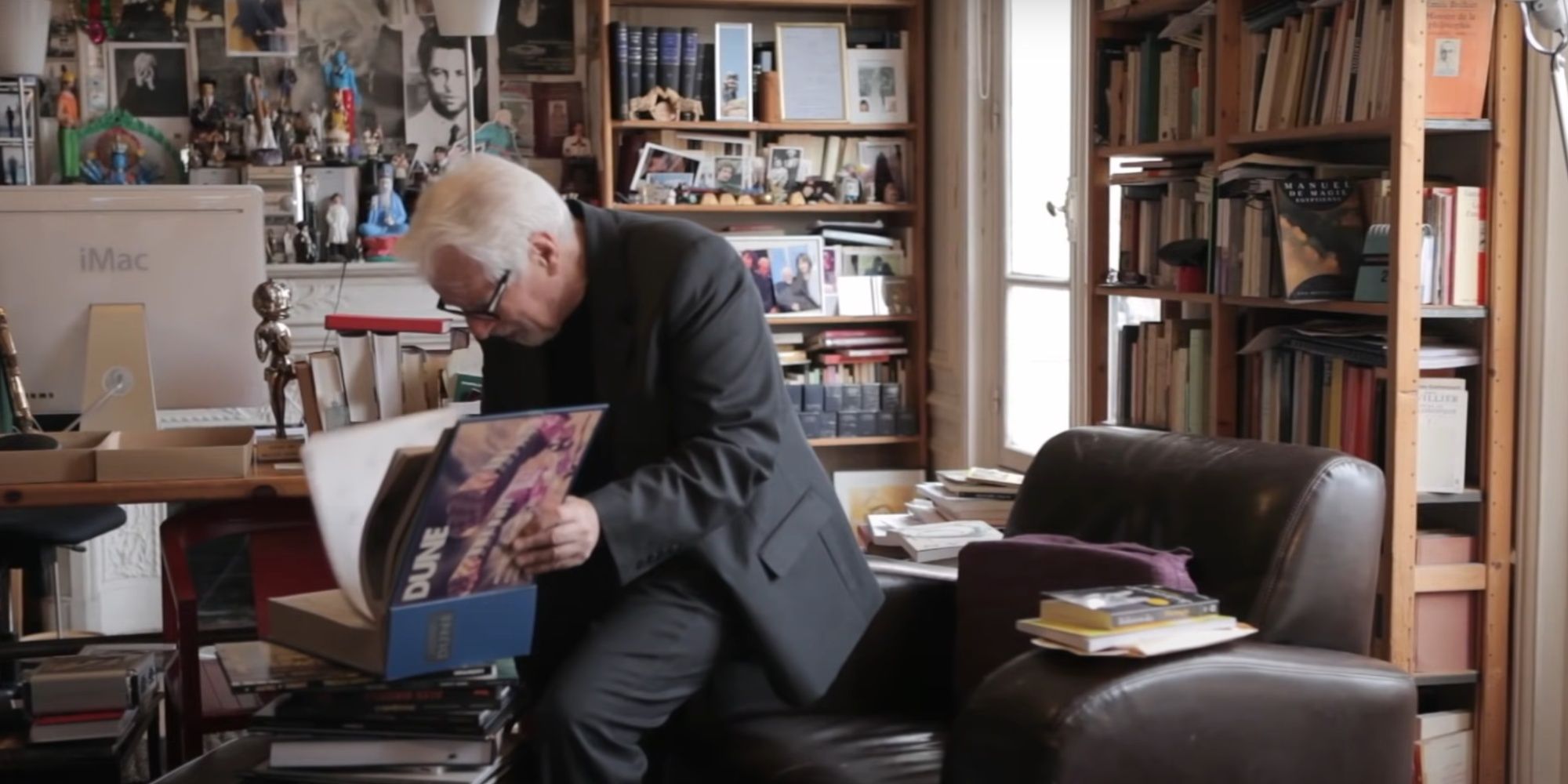 Alejandro Jodorowsky seen sitting in his writer's room and flipping through the pages of his Dune concept handbook.