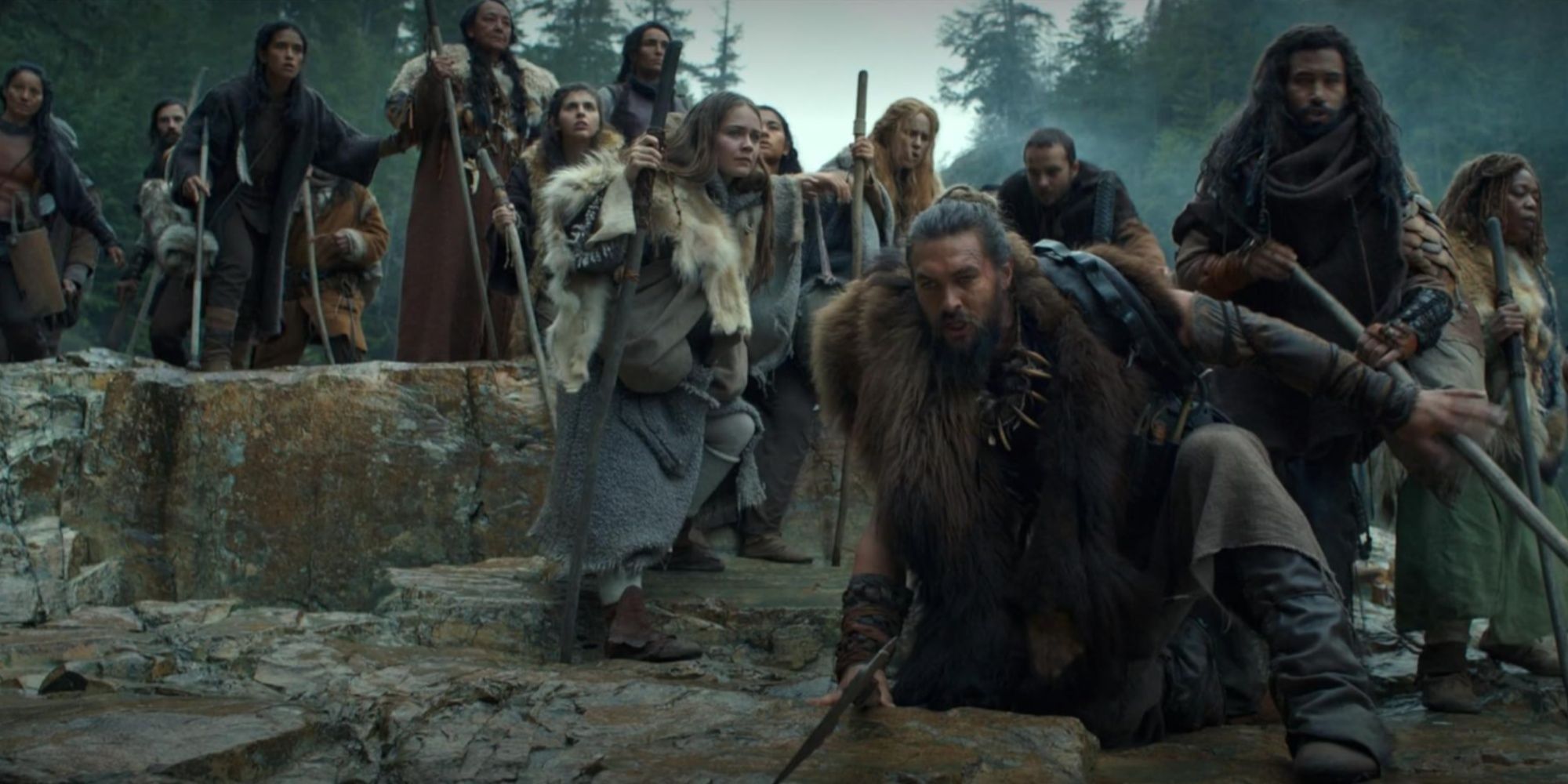 Jason Momoa's character Baba Voss leading his tribe through a rocky path, with his wife Maghra right behind him.