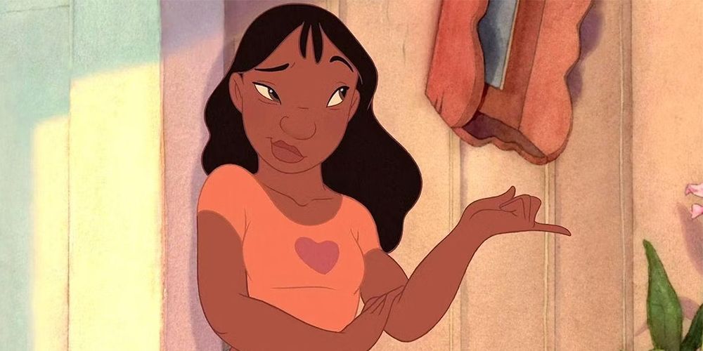 Nani from Lila and Sitich against a wall with a smile as she points to Lily, who is off screen.