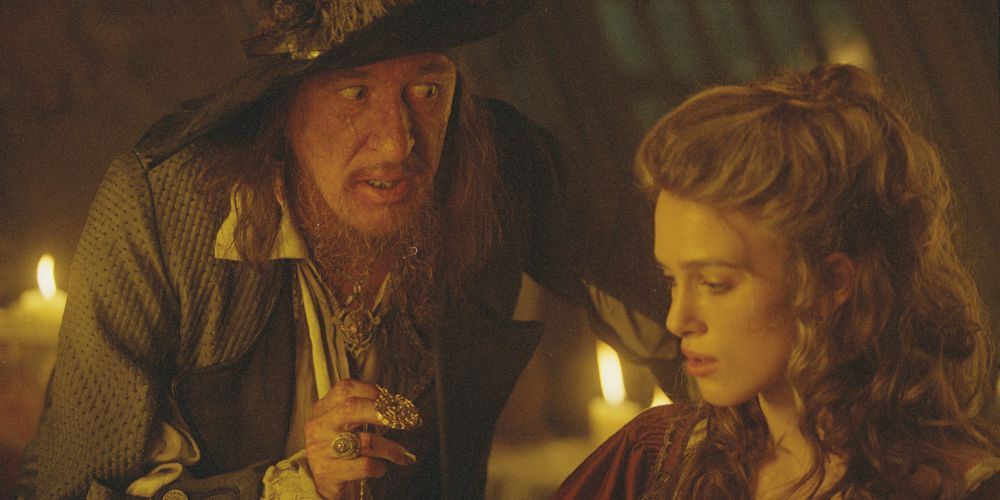 Pirate Captian Barbossa leans over a sitting Elizabeth Swan. 