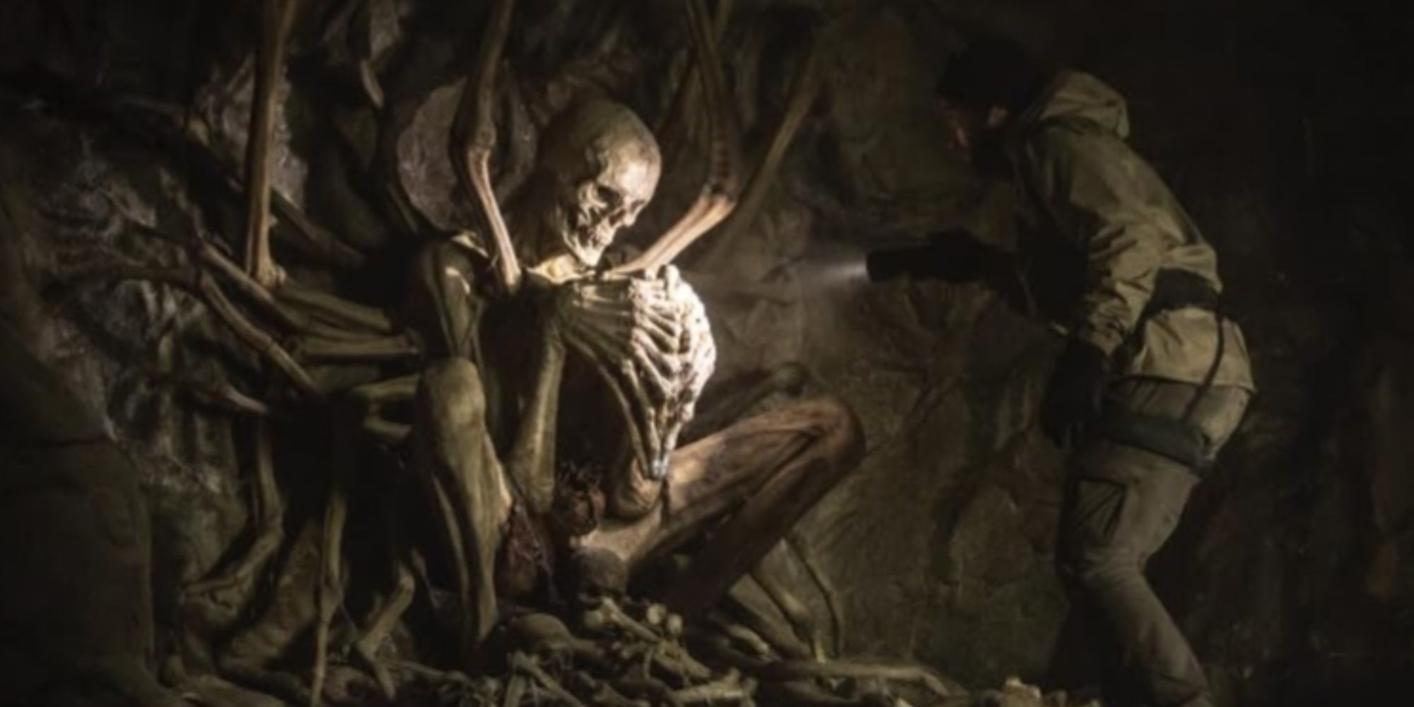 A hiker pointing a flashlight at the large alien-like skeletal structure of the Empty Man figure in an underground cave.