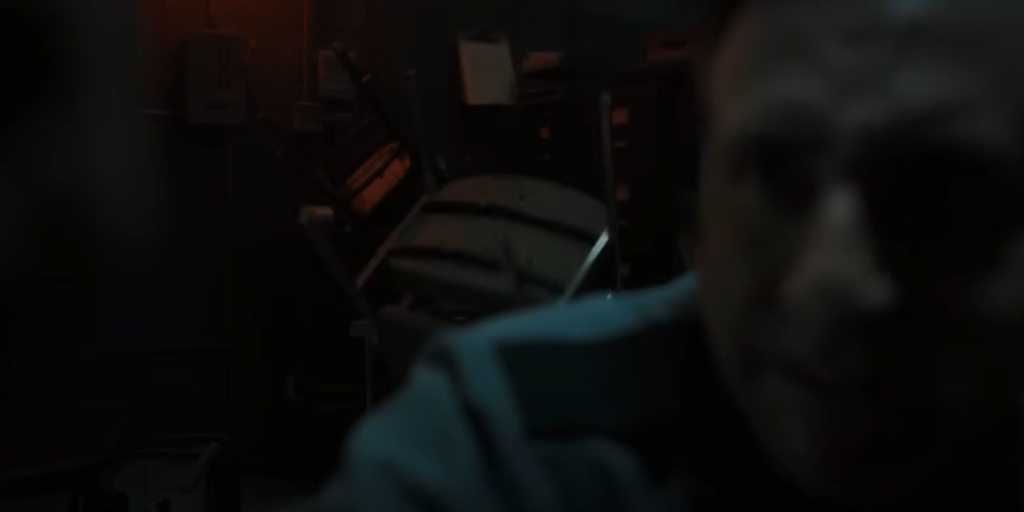 Close-up of the security guard's scared face as he pulls the air vent open and a chair is seen falling in the background.
